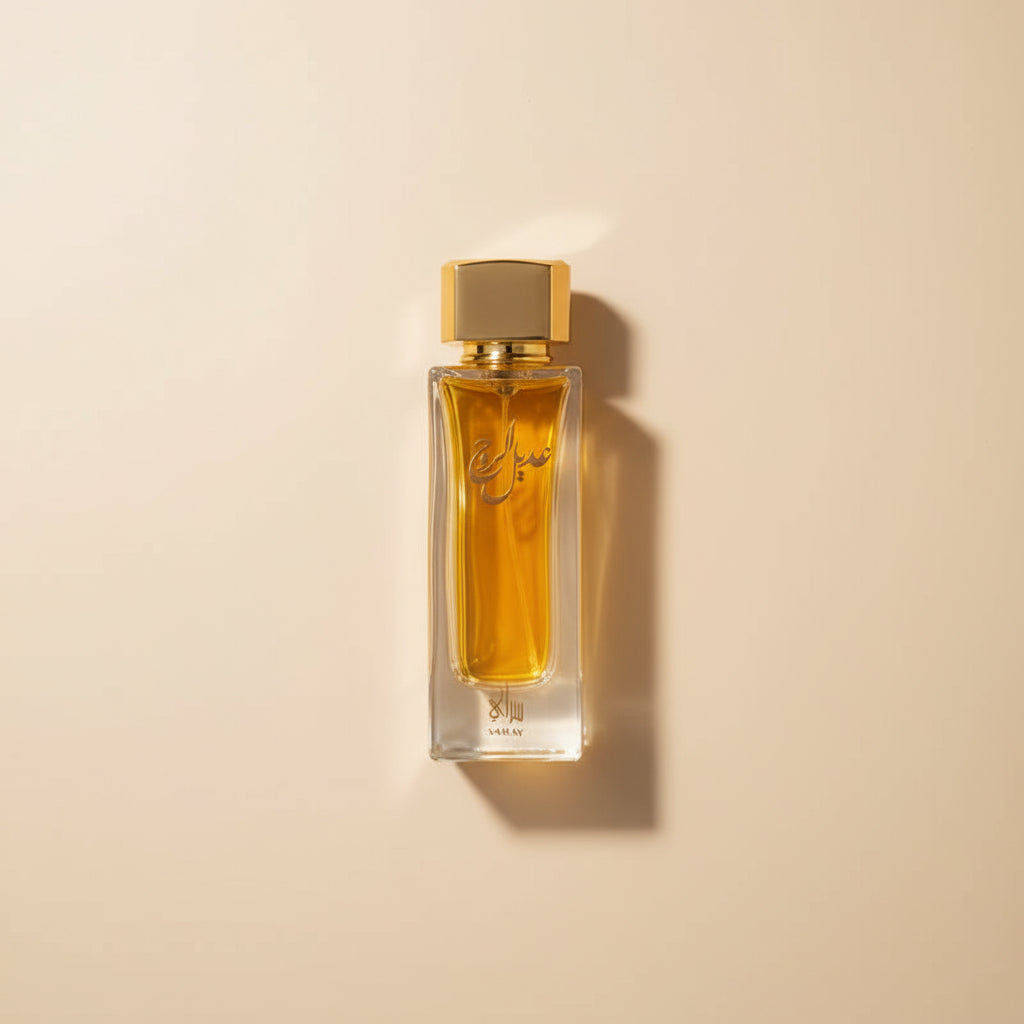 Perfume bottle with gold cap and yellow liquid next to a black box with Arabic text